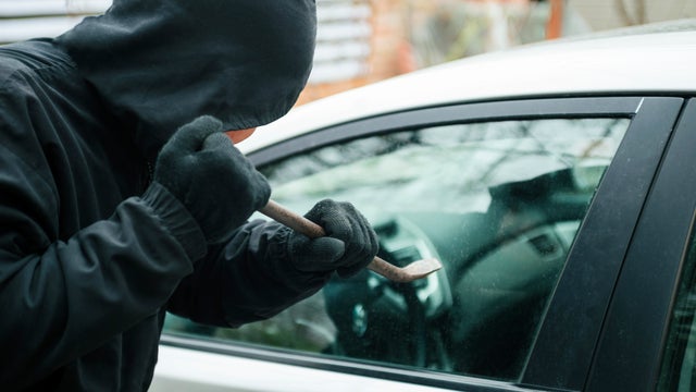 Close-up of a thief wearing balaclava breaking car window with crowbar. Car thief, car theft concept