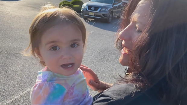 A woman holds a smiling baby, who is looking at the camera 