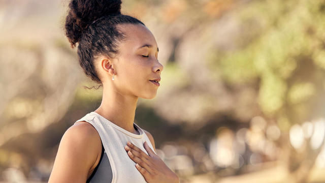 Black woman, breath and hand on chest, for meditation and wellness being peaceful to relax. Bokeh, African American female and lady outdoor, in nature and being calm for breathing exercise and health 