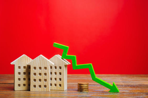 Miniature wooden houses and a green arrow pointing downward. The concept of low-cost real estate. Lower mortgage rates. Falling prices for rental homes and apartments. Declining demand for home purchases 