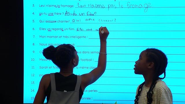 Schoolgirl sitting studying in front of large chalkboard with schoolwork chalked on it 