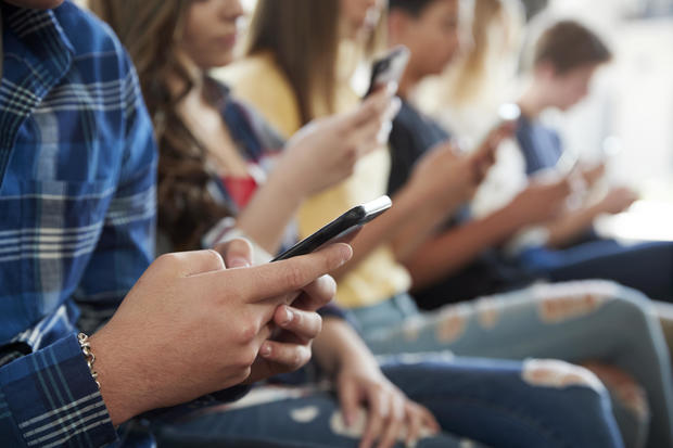 Close Up Of A Line Of High School Students Using Mobile Phones 