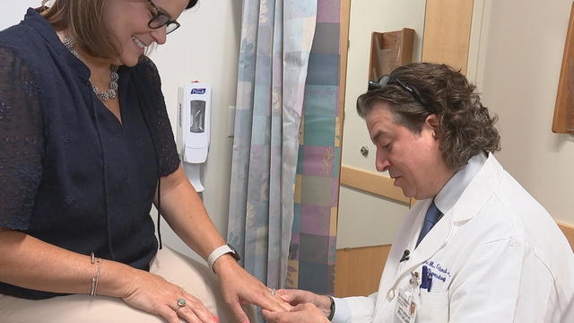 Kelli Amerine speaks to her doctor as he looks at her hands 