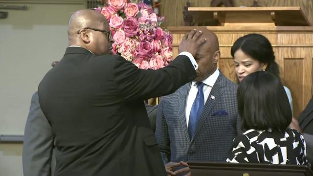 A faith leader places a hand on Mayor Eric Adams' head. 