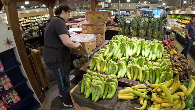 A worker adds bananas to a produce stand in a grocery store 