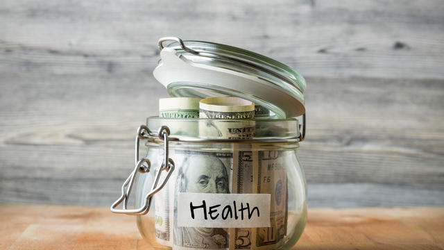 Dollar bills in glass jar isolated on wooden background. Saving money for health. 