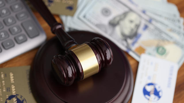 Wooden gavel for judge lies on table next to one hundred dollar bills and bank credit cards. 