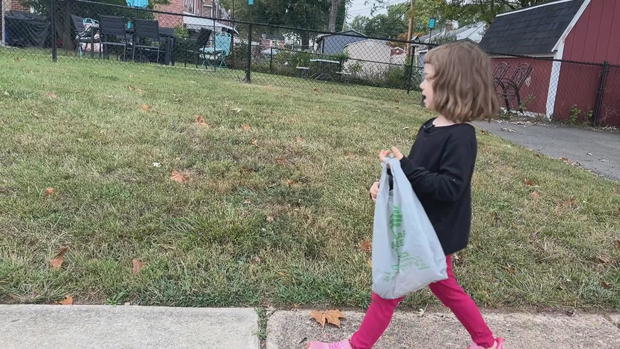 Luna walks on a sidewalk holding a bag to collect trash 