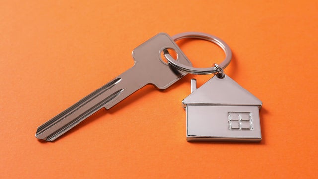 Metallic key with keychain in shape of house on orange background 