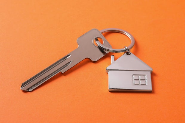 Metallic key with keychain in shape of house on orange background 