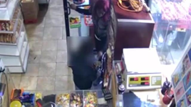 A woman stands in the doorway of a grocery store and talks to a 7-year-old boy, who is holding some cash in his hands. 