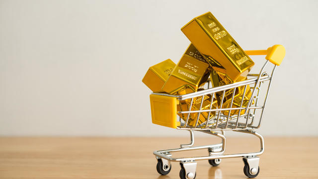 Gold bars in shopping trolley on wooden table with white wall background copy space. 