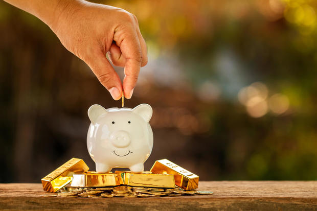 Businessman hand hold a coin is save to the piggy bank put on the gold bar with growing a interest in the public park, Saving money or loan to planning the business investment in the future concept. 