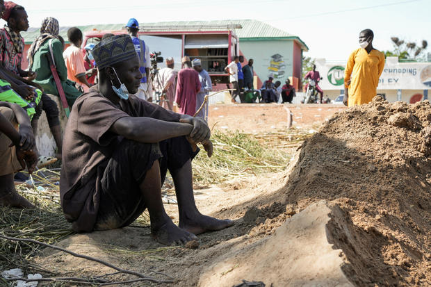 A man sits in front of the graves of the recently buried victims, after a fuel tanker crashed and exploded, in Majia 