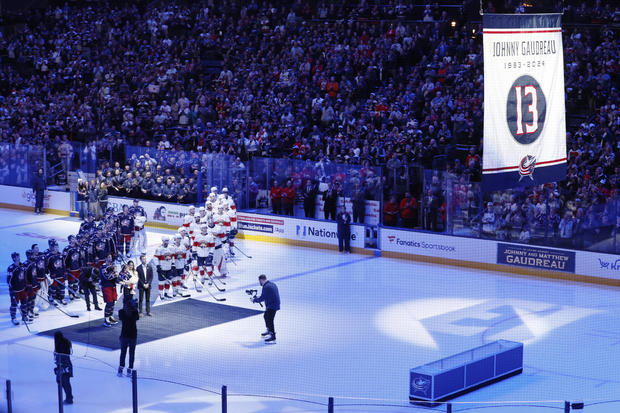 Blue Jackets' Johnny Gaudreau's family and players from both teams stand on the ice to watch a #13 banner being raised during a ceremony before the start of an NHL hockey game between the Columbus Blue Jackets and the Florida Panthers 