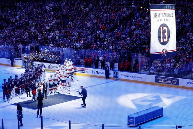 Blue Jackets' Johnny Gaudreau's family and players from both teams stand on the ice to watch a #13 banner being raised during a ceremony before the start of an NHL hockey game between the Columbus Blue Jackets and the Florida Panthers 