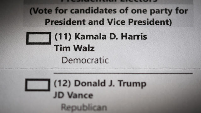 A woman takes a mail-in ballot from an envelope at a polling 