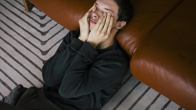 High angle view of man rubbing eyes while reclining on sofa at home 