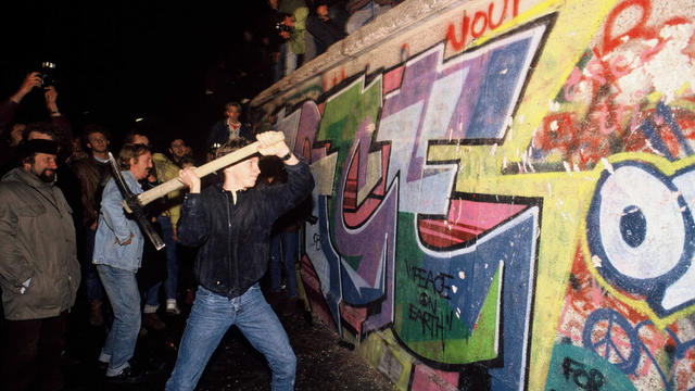 A man attacks the Berlin Wall with a pickaxe on the night of November 9th, 1989 