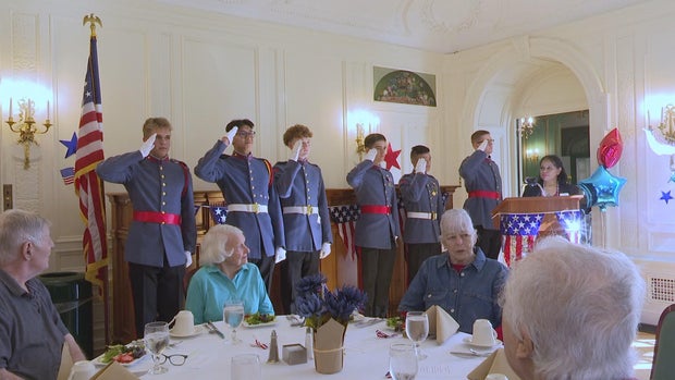 A group of six cadets in uniform salute to a room of older veterans at the Mansion at Rosemont