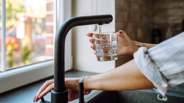 Water filtration in domestic kitchen. Unrecognizable woman hands pouring water in drinking glass from tap 