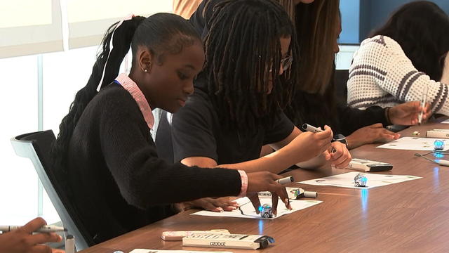 Students work with markers and Ozobots at a conference table 