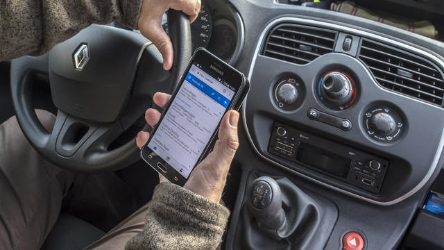 Irresponsible man at steering wheel checking messages on smart phone while driving car on road. 