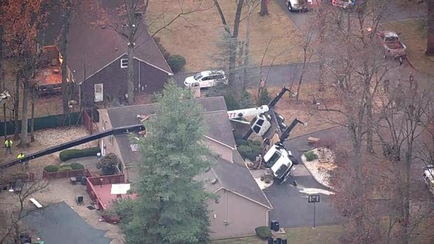 An aerial view of a truck with a crane attached to it on its side with the crane laying across the roof of a home. 