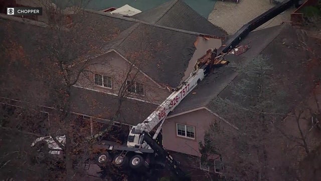 An aerial view of a truck with a crane attached to it on its side with the crane laying across the roof of a home.