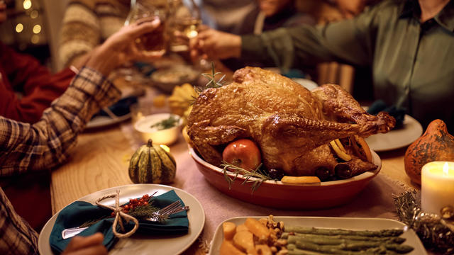 Close up of stuffed turkey during Thanksgiving meal with family toasting in the background. 