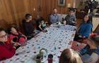 Five adults and four children, three of whom are in wheelchairs, sit around a kitchen table. 