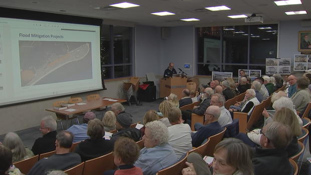 People fill a room during a community meeting, a graphic on the board shows "flood mitigation projects" 