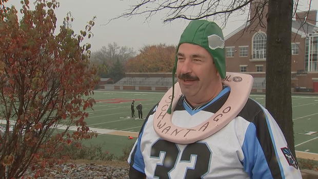 A man speaks to a reporter while wearing a pink toilet seat around his neck 