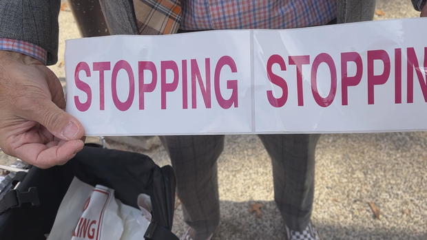 A man holds a roll of stickers that say STOPPING 