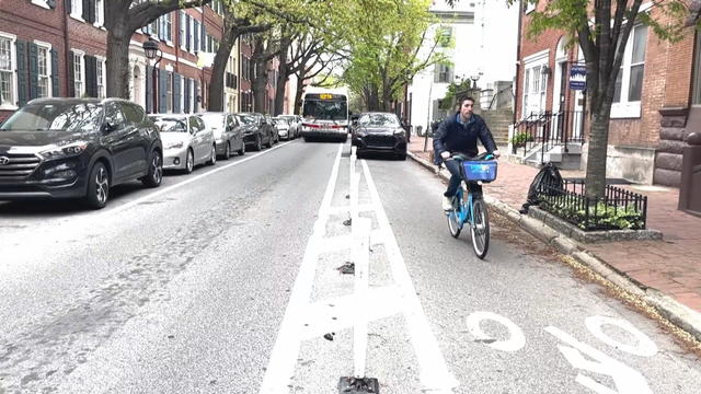 A cyclist rides in the bike lane, which is partly blocked by a car, as a SEPTA bus approaches in the driving lane 