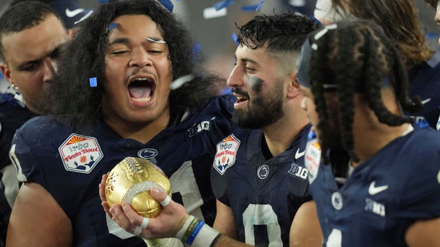 Penn State players celebrate after the Fiesta Bowl College Football Playoff game against Boise State, players are holding a golden football award as blue and white confetti swirls. 