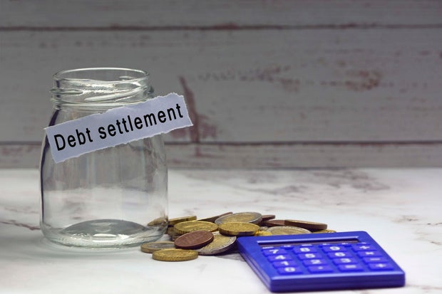 Glass jars with blurred multicurrency coins, calculator and text on white torn paper - Debt settlement