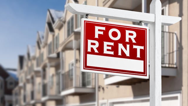 For Rent Real Estate Sign In Front of a Row of Apartment Condominiums Balconies and Garage Doors. 