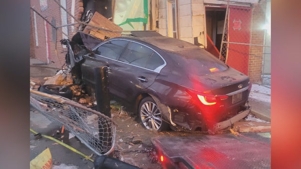 A sedan is seen after it crashed into a building, the building is severely damaged, as is the front of the car
