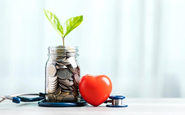 Savings concept for future healthcare. A jar filled with coins and a small plant in the center, accompanied by a heart and a stethoscope, symbolizing saving money for good health in the future