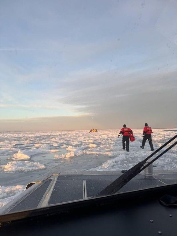 Two Coast Guard crews walk on breaking ice toward an ice fishing spot. 