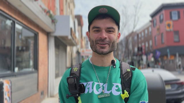 Sami Aziz smiles while talking to a reporter, he's wearing an Eagles sweatshirt and a necklace that looks like a street sign for South Street 