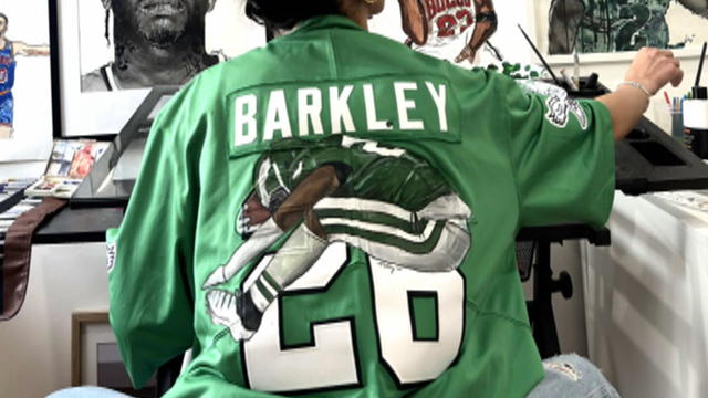 The back of an Eagles jersey with a hand painted picture of Saquon Barkley's backward hurdle painted over part of the numbers 