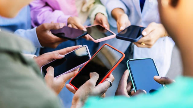 Young group of people standing in circle using mobile phones outside. Unrecognizable teen friends watching social media content on smartphone app. Technology lifestyle concept. 