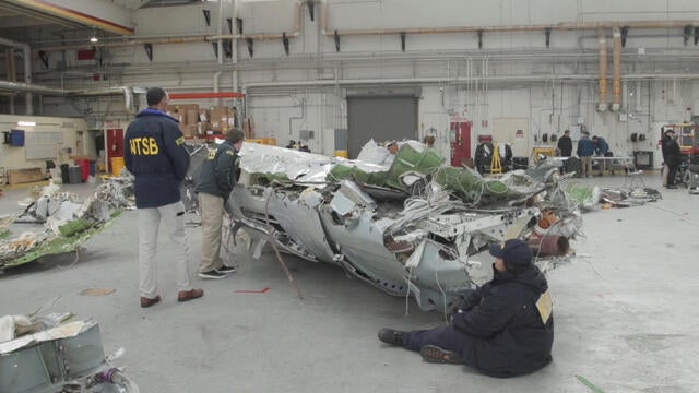 Members of the National Transportation Safety Board examine the wreckage from the midair collision of American Eagle Flight 5342 and a Black Hawk helicopter, kept in a hangar at an unknown location, in this image capture from handout video released Feb. 8 