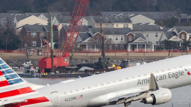 Recovery teams lift the mangled remains of a military helicopter that crashed midair with an American Airlines commercial airplane from the Potomac River as an American Airlines plane takes off from Ronald Reagan International Airport in Arlington, Virginia, on Feb. 6, 2025. 