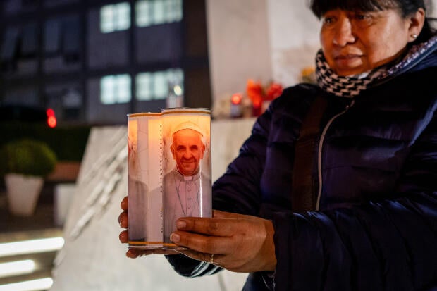 A woman carries two candles with the image of Pope Francis