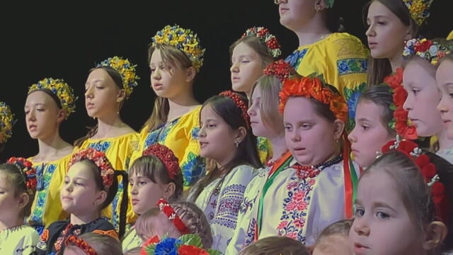 Children wearing traditional Ukrainian clothing sing during an event 