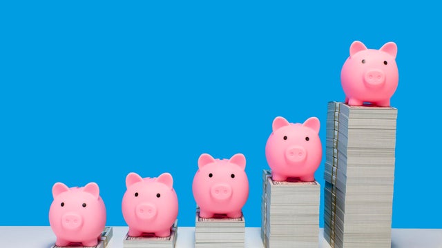 Pink piggy banks on ascending stacks of paper currency 