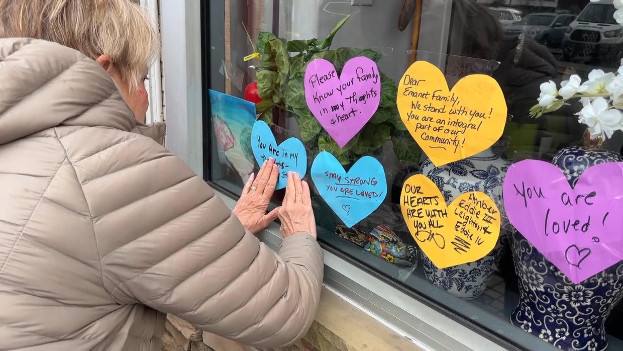 A woman tapes a heart with a message onto the window of Jersey Kebab, there are other paper hearts there with messages of support, one says "you are loved" 